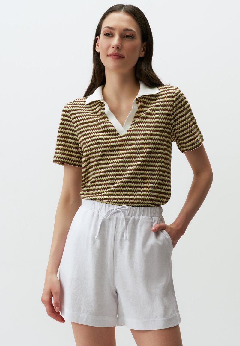 Camicia con colletto in un motivo zigzag marrone, giallo e verde, abbinata a pantaloni corti bianchi con coulisse. Texture liscia e vestibilità rilassata.