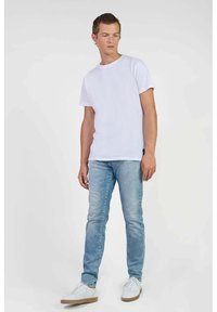 Witte t-shirt met korte mouwen gecombineerd met lichtblauwe jeans. Het shirt is eenvoudig, terwijl de jeans een vervaagde wassing hebben. De schoenen zijn witte sneakers.
