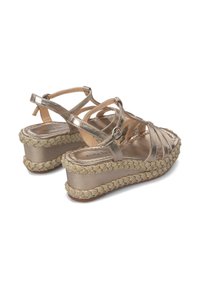 Sandalias de cuña metálicas en color dorado con tiras entrecruzadas, textura trenzada en la suela y un adorno de cuentas decorativas alrededor de la base.
