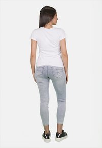 T-shirt bianca a maniche corte abbinata a jeans skinny blu chiaro. I jeans presentano sottili design sui taschini posteriori e sono completati da sneakers nere.