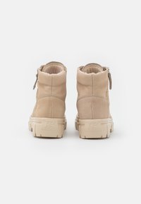 Bottines en cuir beige avec une finition texturée, dotées d'une fermeture éclair sur le côté et d'une semelle en caoutchouc beige épaisse.