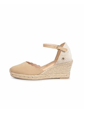 Alpargata cuña beige con parte delantera festoneada, hebilla en la correa del tobillo y panel del talón tejido con textura.