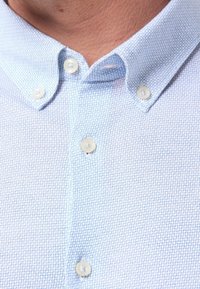 Jasnoniebieska koszula na guziki z teksturowanej tkaniny, z kołnierzykiem i białymi guzikami, z delikatnym wzorem siatki.