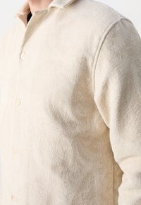 Beige texturerad skjorta med knapp-up och ett subtilt mönster, med krage och ljusa knappar.