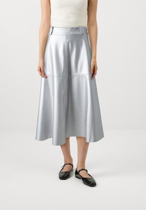 La falda midi de imitación cuero plateado presenta una textura suave, forma en A y detalles de costura visibles, combinada con zapatos de tacón cuadrado negros.