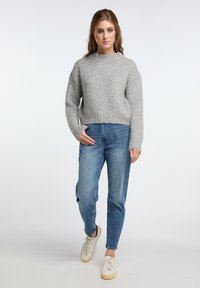 Maglione grigio a maglia con un motivo testurizzato, abbinato a jeans blu a gamba dritta e sneakers bianche. Il maglione ha un design corto e maniche lunghe.