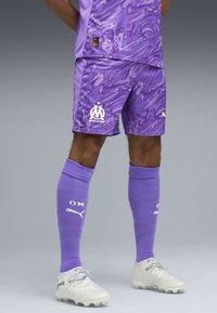 Maglia da calcio viola con motivi astratti, logo del club bianco, e calzettoni abbinati con accenti bianchi. Design chiaro e dettagli testurizzati.