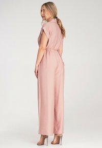 Różowa kombinezon w odcieniu blush z krótkimi rękawami, paskiem w talii i szerokimi nogawkami. Gładki materiał, detal kołnierzyka i widoczna szew z tyłu.