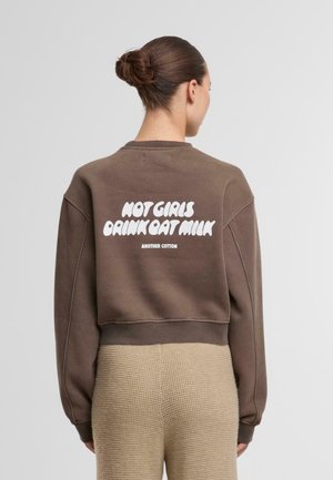 Brązowa krótka bluza z białym napisem "NOT GIRLS DRINK OAT MILK" na plecach. Miękka w dotyku, z ściągaczami na mankietach i przy dekolcie. Prosty design.