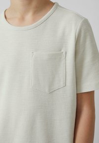 Lichtgrijs T-shirt met korte mouwen, gemaakt van een gestructureerde stof, met een borstzak en een ronde halslijn. Minimalistisch ontwerp met subtiele details.