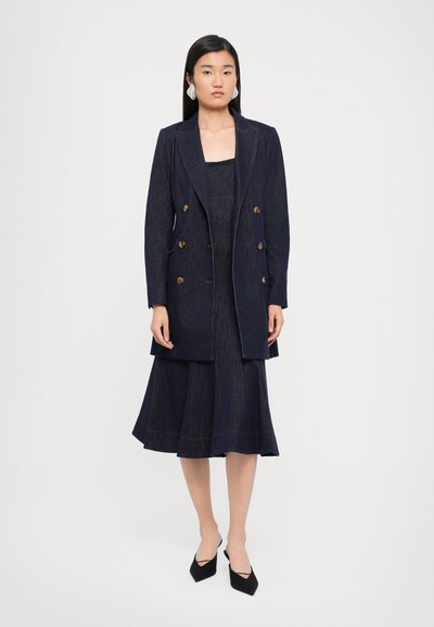 Donkerblauwe dubbelgebreide blazer met gouden knopen, gecombineerd met een bijpassende aansluitende jurk die uitloopt bij de knie, met subtiele textuur.