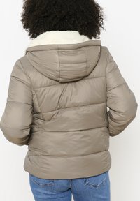 Khaki péřová bunda s bílou, plyšovou podšívkou kapuce. Má prošívanou strukturu a elastické manžety. Zadní strana má zaoblený lem a horizontální švy.