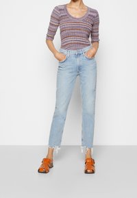 Ljusblå denimjeans med rak passform och fransad nederkant, matchade med en lila och orange randig stickad topp och orange sandaler med remmar.