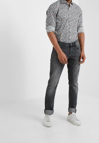 Camicia a maniche corte con motivo floreale, con maniche arrotolate, abbinata a jeans denim grigi e sneakers bianche. Stile casual, vestibilità moderna.