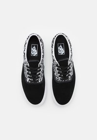 Svarta canvas sneakers med vita accenter, med ett mönstrat krage, snördesig och gummisulor. Klassisk Vans-logotyp synlig inuti.