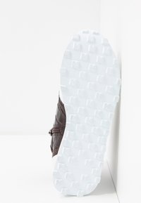 Chaussure en cuir marron avec un dessus texturé et une semelle en caoutchouc blanche à clous. Le talon présente un détail de couture distinctif.