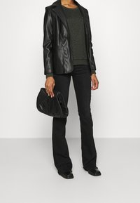Blazer in pelle nera sopra un maglione testurizzato verde scuro, abbinato a jeans neri a zampa e una borsa nera trapuntata. Scarpe nere flat.