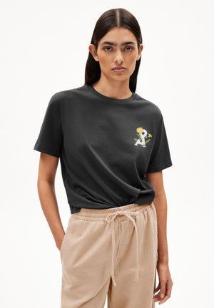 T-shirt en coton noir à manches courtes avec un graphisme floral coloré sur la poitrine gauche. Associé à un pantalon beige à cordon de serrage.