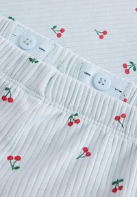 Tissu blanc avec des rayures horizontales, présentant un motif de petites cerises rouges et de feuilles vertes. Comprend un bouton bleu et une taille élastique.