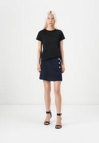 Black short-sleeve t-shirt paired with a navy tweed mini skirt featuring three gold buttons on the side. Black heeled sandals complete the look.
