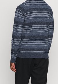 Pletený svetr v odstínech modré s horizontálními pruhy, s žebrovaným lemem a manžetami. Vyrobeno z měkkého textilního materiálu.