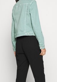 Mintgrön denimjacka med kort skärning, knäppta manschetter och detaljer i metall. Matchad med lösa svarta byxor.