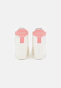 Sneakers bianche con design alto alla caviglia, con accenti rosa sul tallone e sul lato. Il nome del marchio "GUESS" è visibile sul retro.