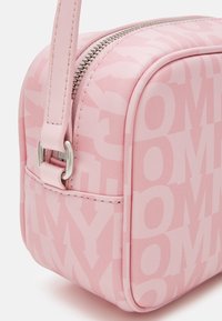 Różowa torba z ekoskórki z górnym suwakiem, tłoczonym wzorem logo oraz regulowanym paskiem. Posiada zaokrąglone rogi i srebrne akcenty.