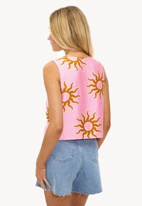 Top corto de tirantes en tela rosa con diseños de soles amarillos, con un escote redondo y sin mangas, combinado con shorts de mezclilla.