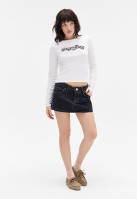 White long-sleeve top with graphic design; dark denim mini skirt with pinstripes; beige shoes and light pink socks are worn.