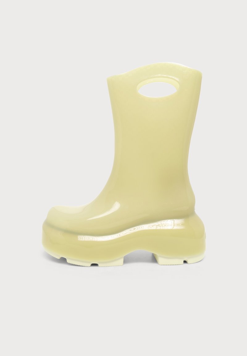 Botte en caoutchouc jaune pâle à tige haute, semelle épaisse et découpe intégrée en haut pour faciliter l'enfilage.