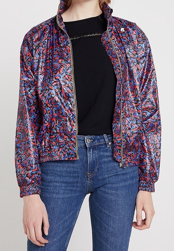 Veste bomber colorée et à motifs avec une finition brillante, présentant une fermeture éclair à l'avant, des poignets en côtes et une ceinture en côtes. Portée par-dessus une chemise noire.