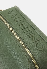 Bolso de cuero verde oscuro con superficie texturizada, que presenta un prominente logo grabado "VALENTINO" y un detalle de cremallera dorada.