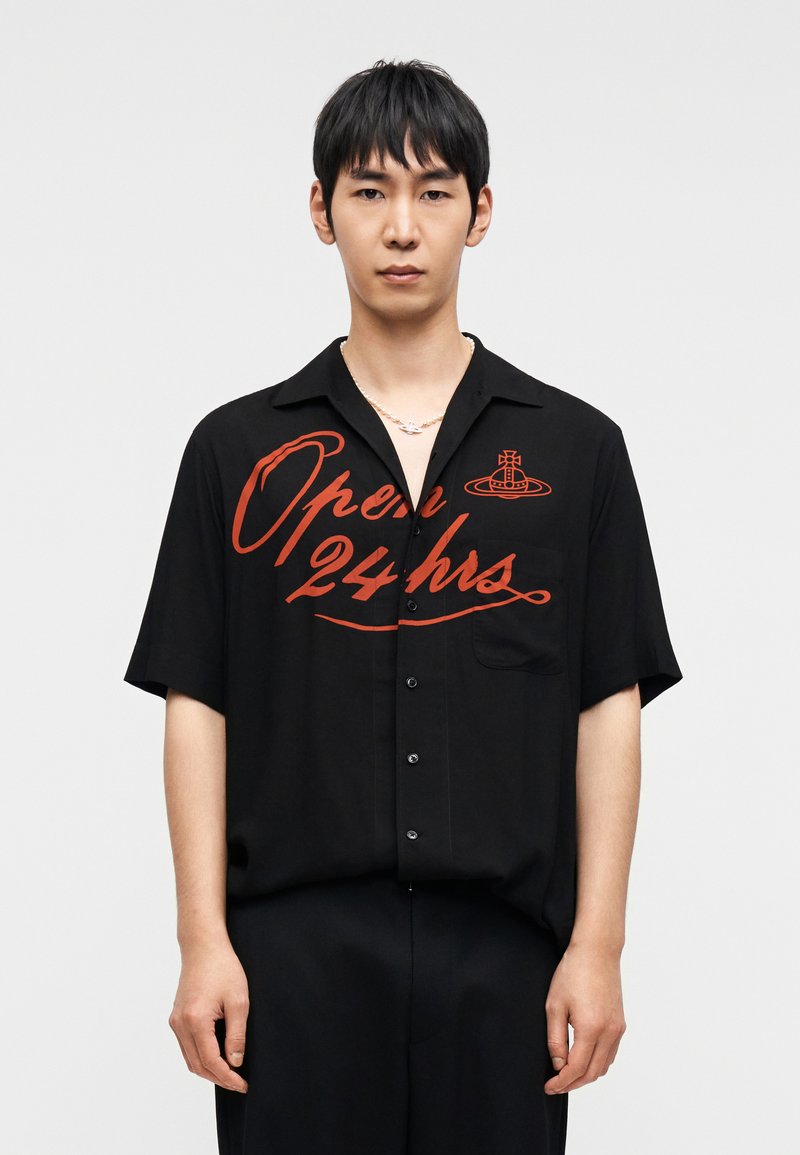 Chemise noire à manches courtes avec inscription rouge "Ouvert 24 h/24" et logo. Présente un design à boutons et une poche poitrine unique.