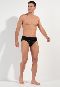 Zwarte boxershorts met een patroon, voorzien van kleine zilveren stippen. Elastische tailleband en gladde stof. Model staat blootsvoets.