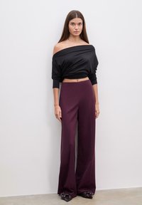 Sort off-shoulder top og viddebenede bordeauxbukser. Bukserne har et glat, tekstureret stof, mens toppen hænger løst.