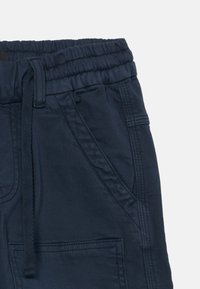 Pantaloni con cintura elastica blu navy, dotati di un cordoncino, tasche laterali e dettagli di cucitura in evidenza. Tessuto liscio e texturizzato.