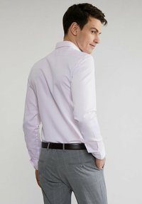 Jasnoróżowa koszula z długim rękawem i kołnierzykiem zapinanym na guziki, z teksturowanej powierzchni; zestawiona z jasnoszarymi spodniami w kratę i czarnym paskiem.