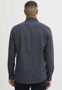 Mørkegrå langermet skjorte laget av teksturert stoff, med en klassisk krage, knappedetaljer ved ermene og en buet nederkant.