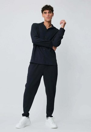 Ensemble de vêtements d'intérieur bleu marine comprenant un haut boutonné avec col et un pantalon assorti à coupe fuselée, associé à des baskets blanches. Texture de tissu doux.