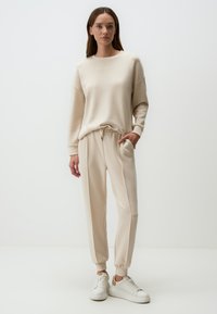 Beige sweater en jogger in een zachte, gestructureerde stof. De top heeft een ronde halslijn en verlaagde schouders; de joggers hebben een elastische tailleband en zakken.