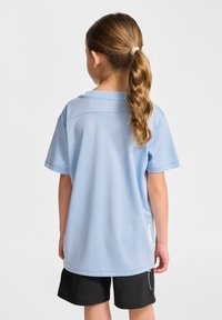 Ljust blå kortärmad skjorta med rund halsringning och en söm på bakstycket. Matchad med svarta shorts. Tyget ser slätt och lättviktigt ut.