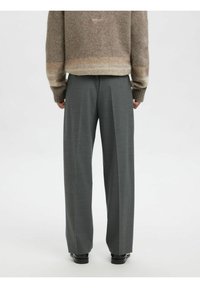 Pelēkas, platā stila bikses ar gludu tekstūru un gludinātām krokām, kombinētas ar brūnu pūkainu džemperi ar gradienta dizainu.