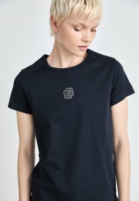 Mørkeblå bomulls T-skjorte med rund hals og korte ermer, med et glitrende 'B' logo i rhinestones på brystet.