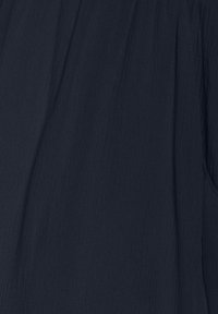 Mörkblå tyg med en texturerad yta, med subtila veck och ett mjukt fall, idealiskt för mångsidig styling och komfort.