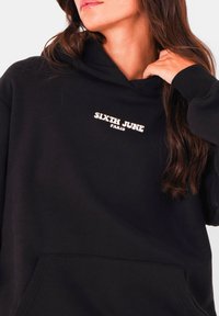 Zwarte hoodie met een vooraanstaande kangoeroe zak. De stof is zacht, met een logo "SIXTH JUNE PARIS" in het wit op de borst. Voorzien van een capuchon met trekkoord.