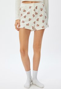 Hvide bomulds shorts med et gentaget brunt bamseprint, med knaplukning og en afslappet pasform, parret med hvide sokker.