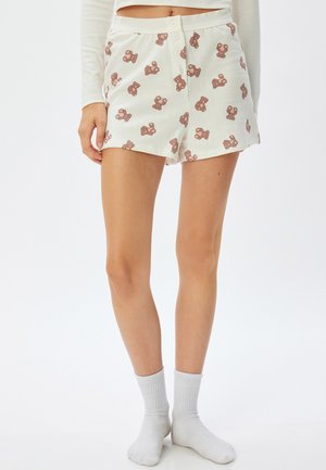 Witte katoenen shorts met een herhaald bruin teddybeerprint, voorzien van een knoopsluiting en een relaxte pasvorm, gecombineerd met witte sokken.