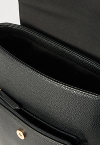 Μαύρη δερμάτινη τσάντα χειρός με υφή, τσέπη με φερμουάρ και μαγνητικό κλείσιμο. Εσωτερική επένδυση με λείο φινίρισμα.