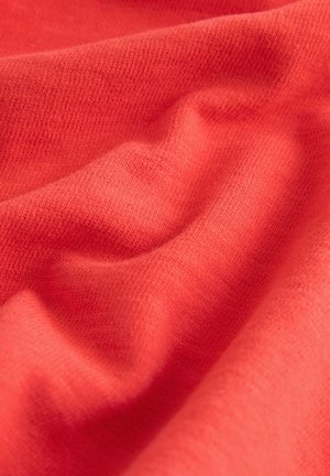 Korallenfarbener Stoff mit einer glatten Textur, der weiche Falten und ein feines Strickmuster aufweist. Das Licht reflektiert dezent und betont seine lebendige Farbe.